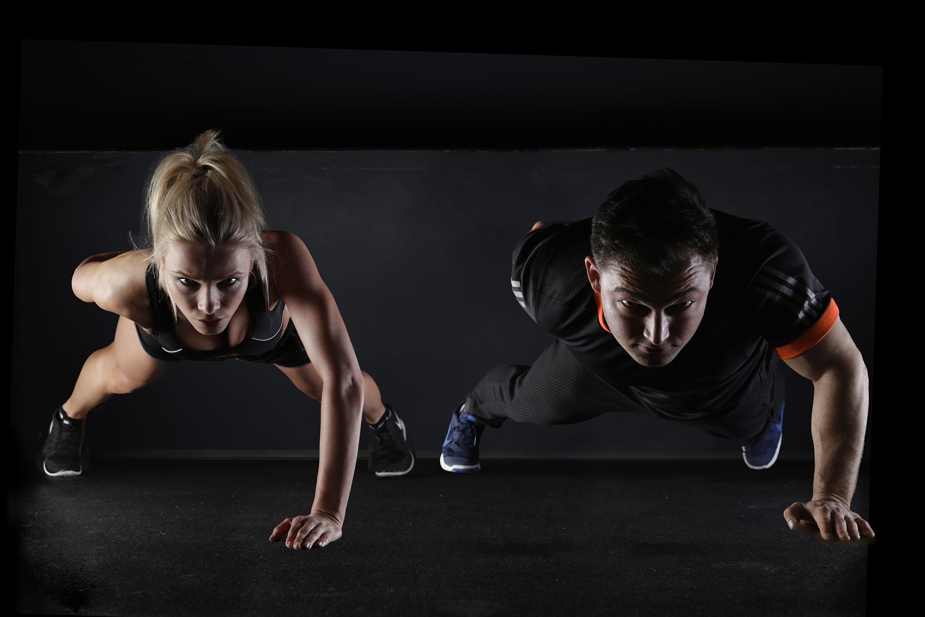 Woman and man doing a one-hand pushup in a black room