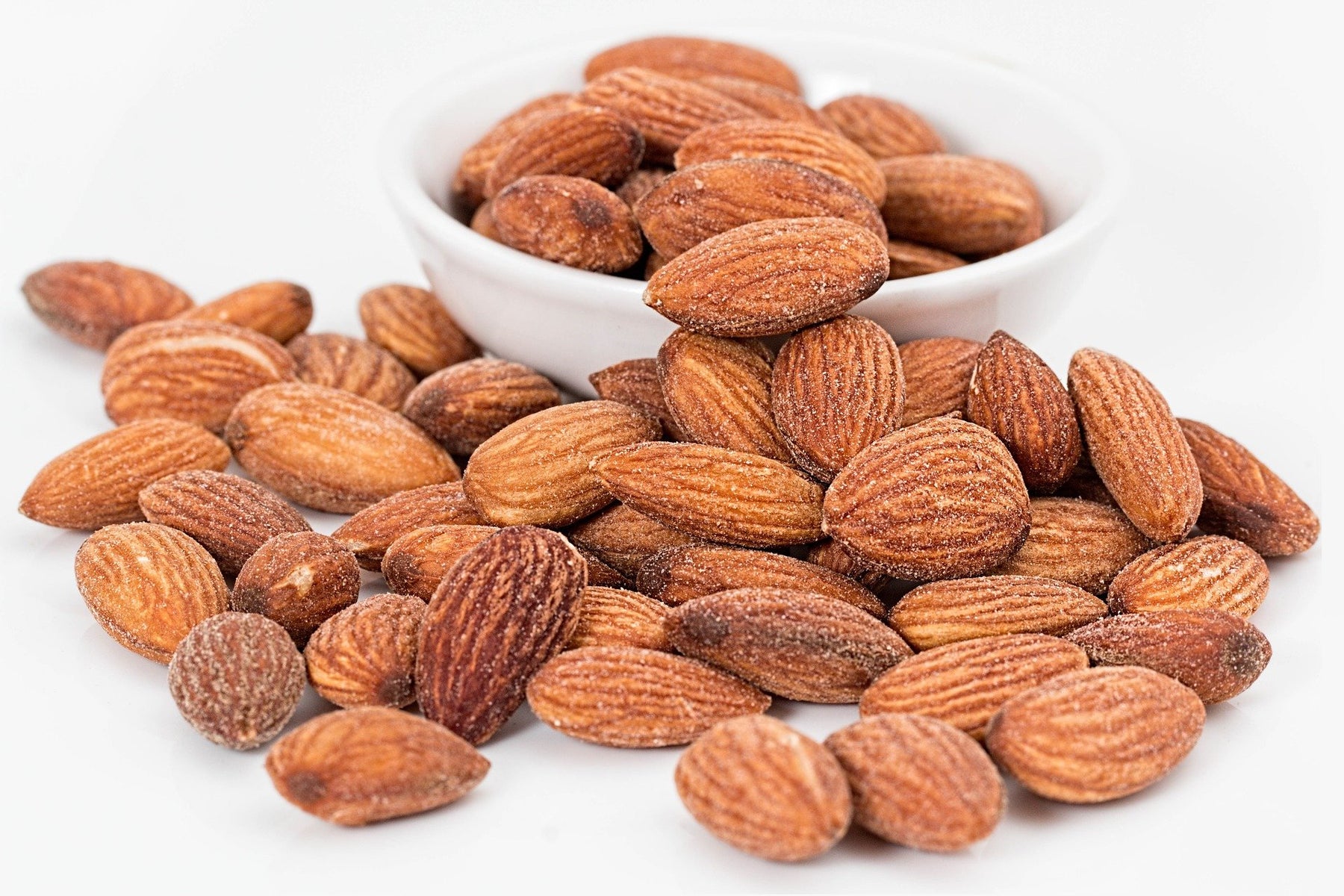 Almonds on a table next to almonds in a white small bowl