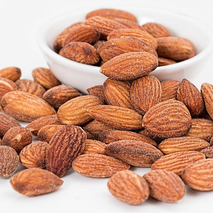 Almonds on a table next to almonds in a white small bowl