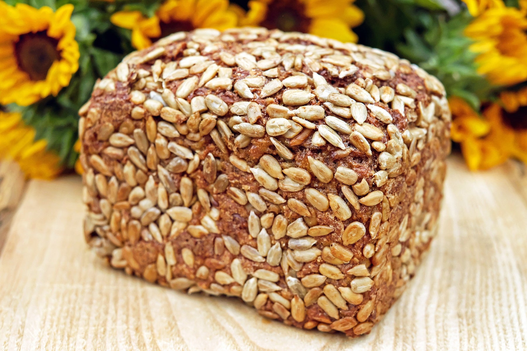 Bread with seeds on a wooden table and sunflowers in the back