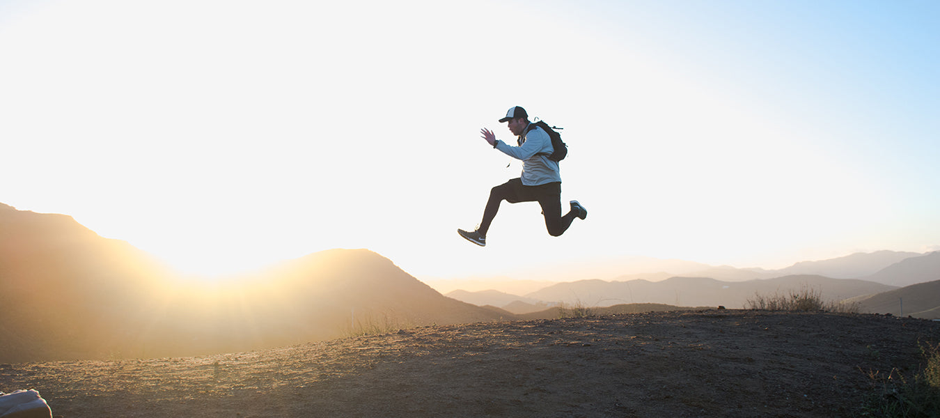 Man with backpack jumping over mountains