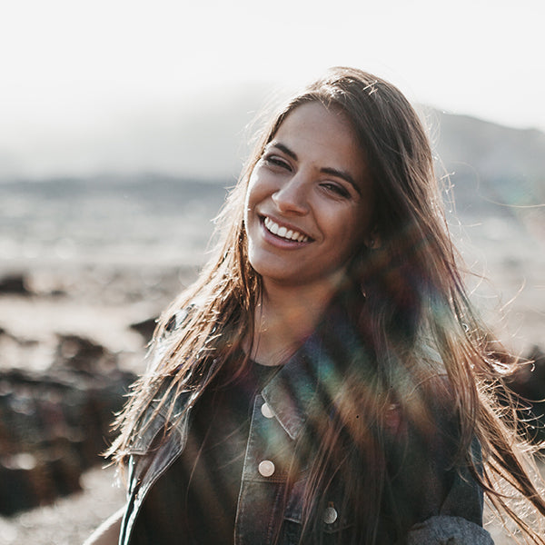 Brunette woman smiling with a mountain and sun behind her