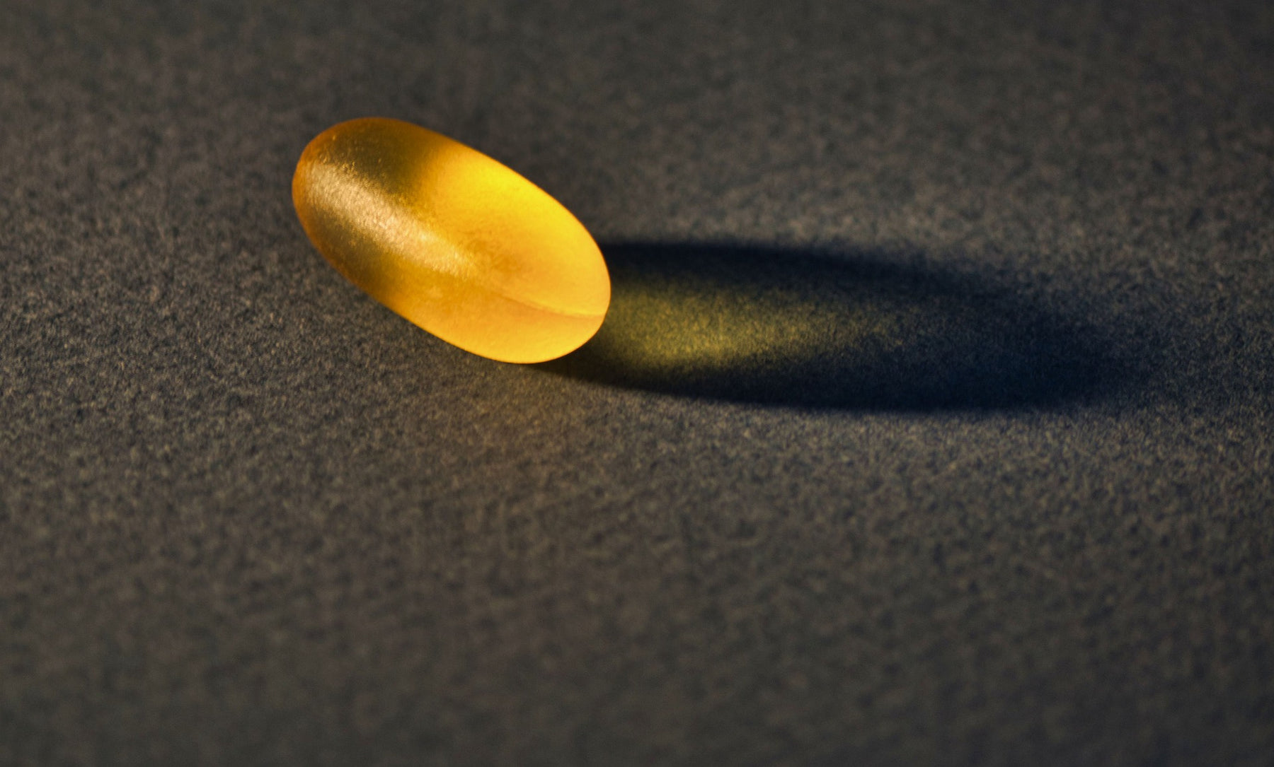 On pill and its shadow on a black surface