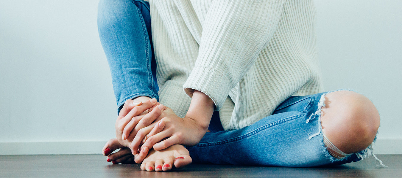 Woman in white sweater and blue jeans massaging her foot