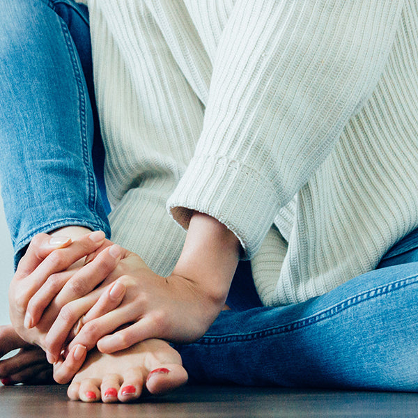 Woman in white sweater and blue jeans massaging her foot