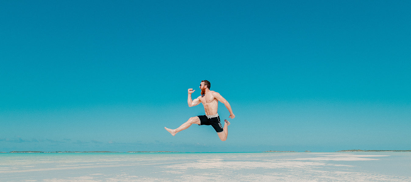 Shirtless man jumping in desert over a blue sky