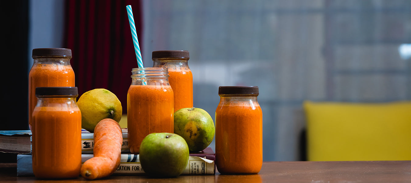 Healthy juices looking orange over five jars surrounded by fruits and vegetables