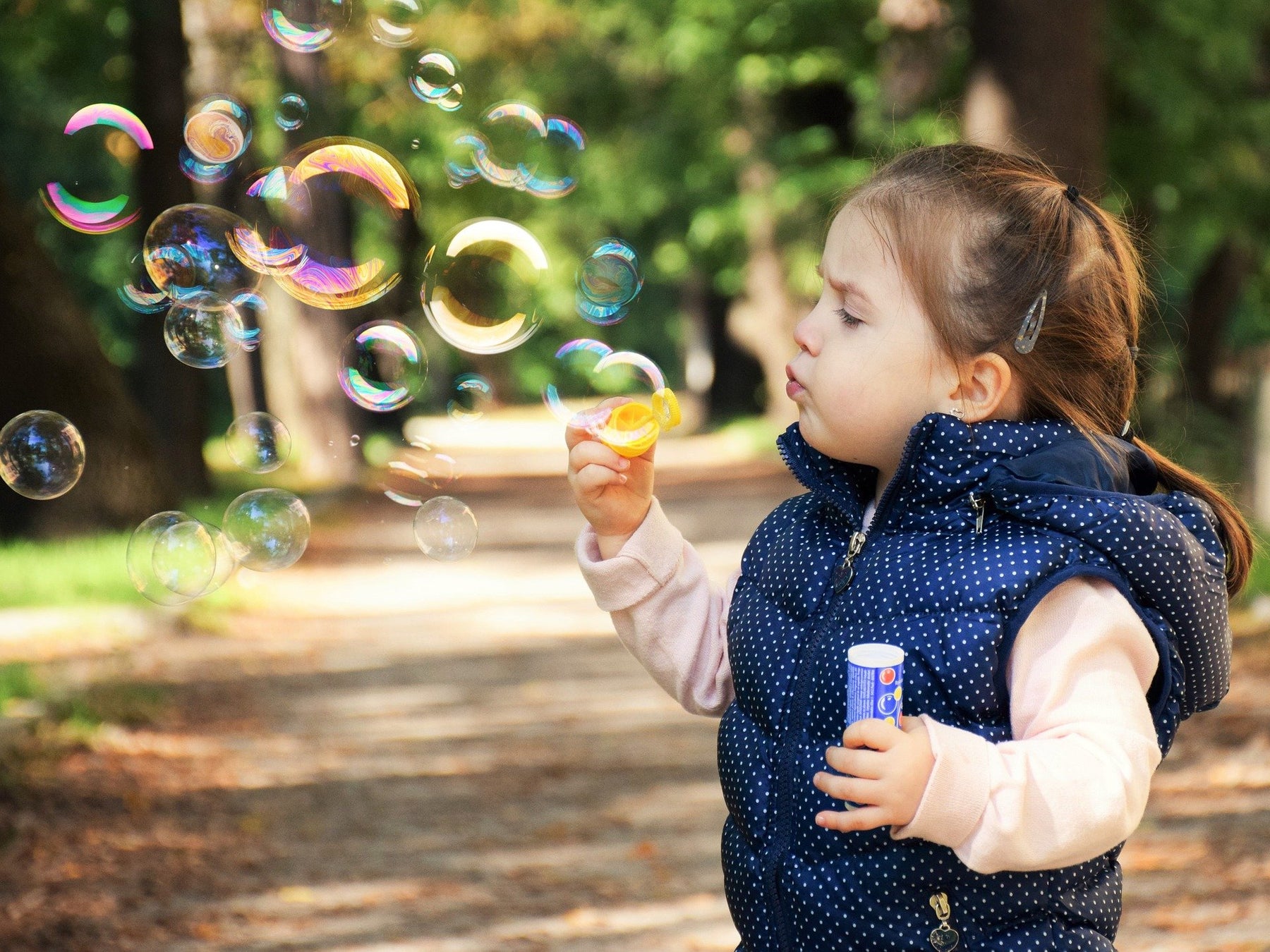 Kid dressed on blue creating soap bubbles in nature