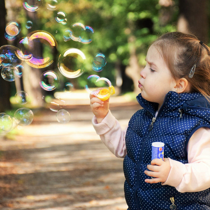 Kid dressed on blue creating soap bubbles in nature