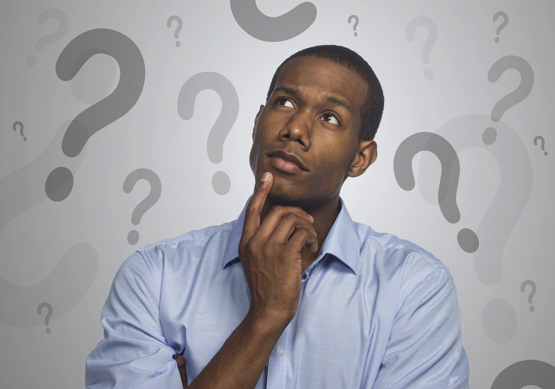 Man in a shirt with his head up thinking surrounded by question marks