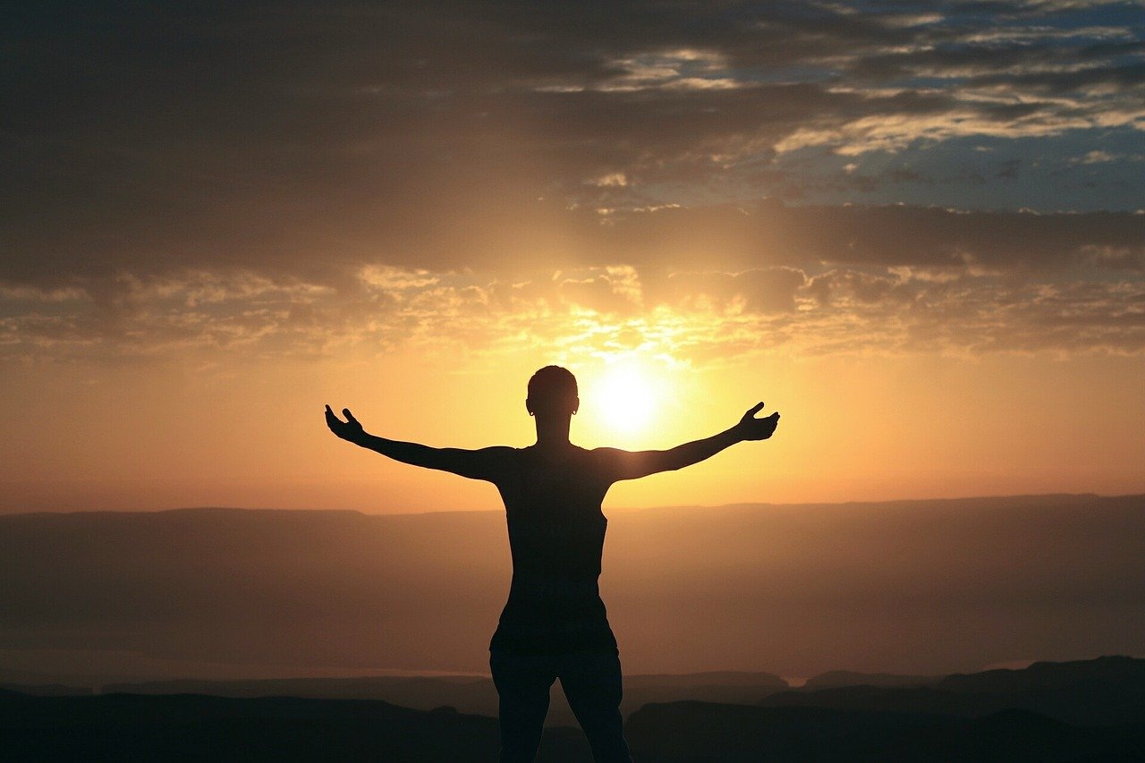 Woman looking at a sunrise with her hands pointed up