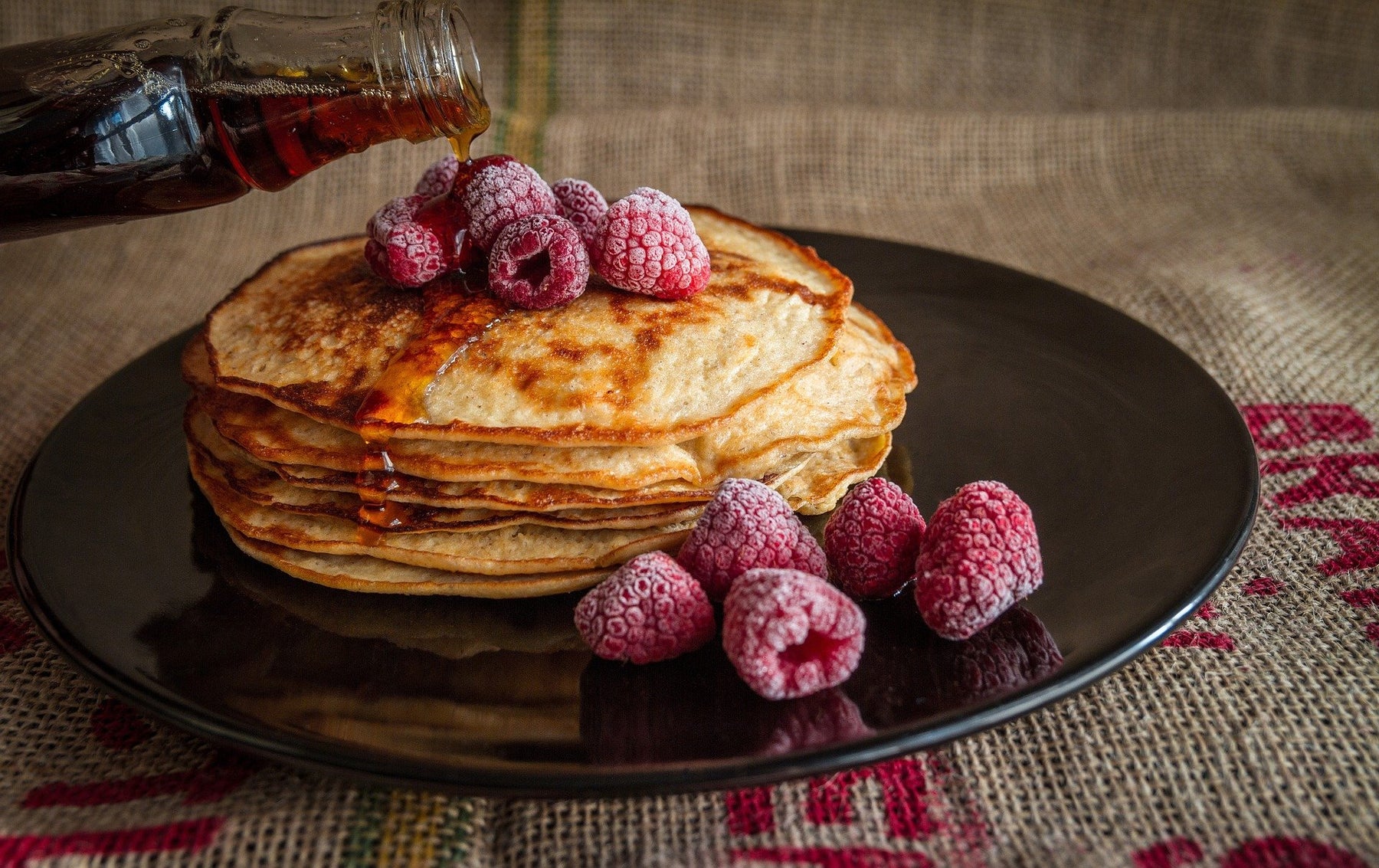 Syrup pouring over pancakes topped with raspberries
