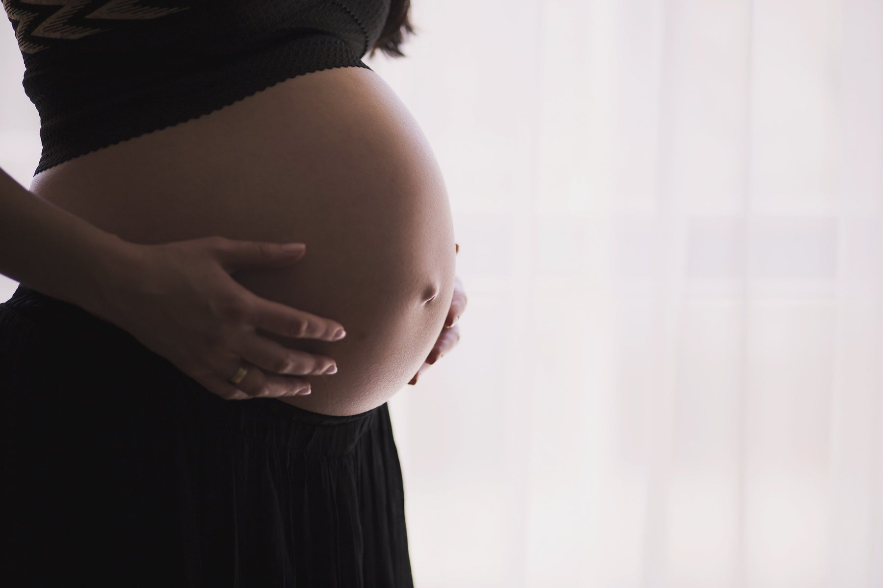 Pregnant woman wearing black with hands over the belly