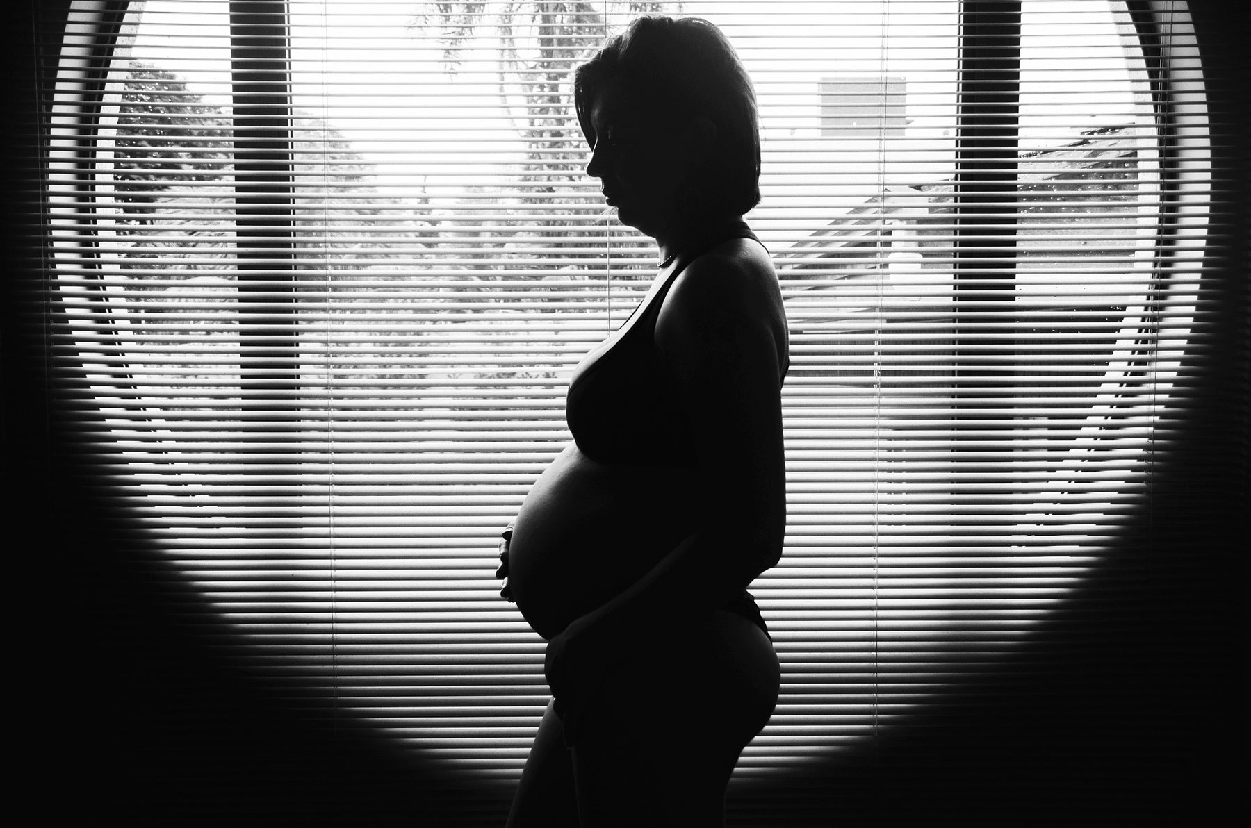 Pregnant woman sitting in a dark room with windows in the middle