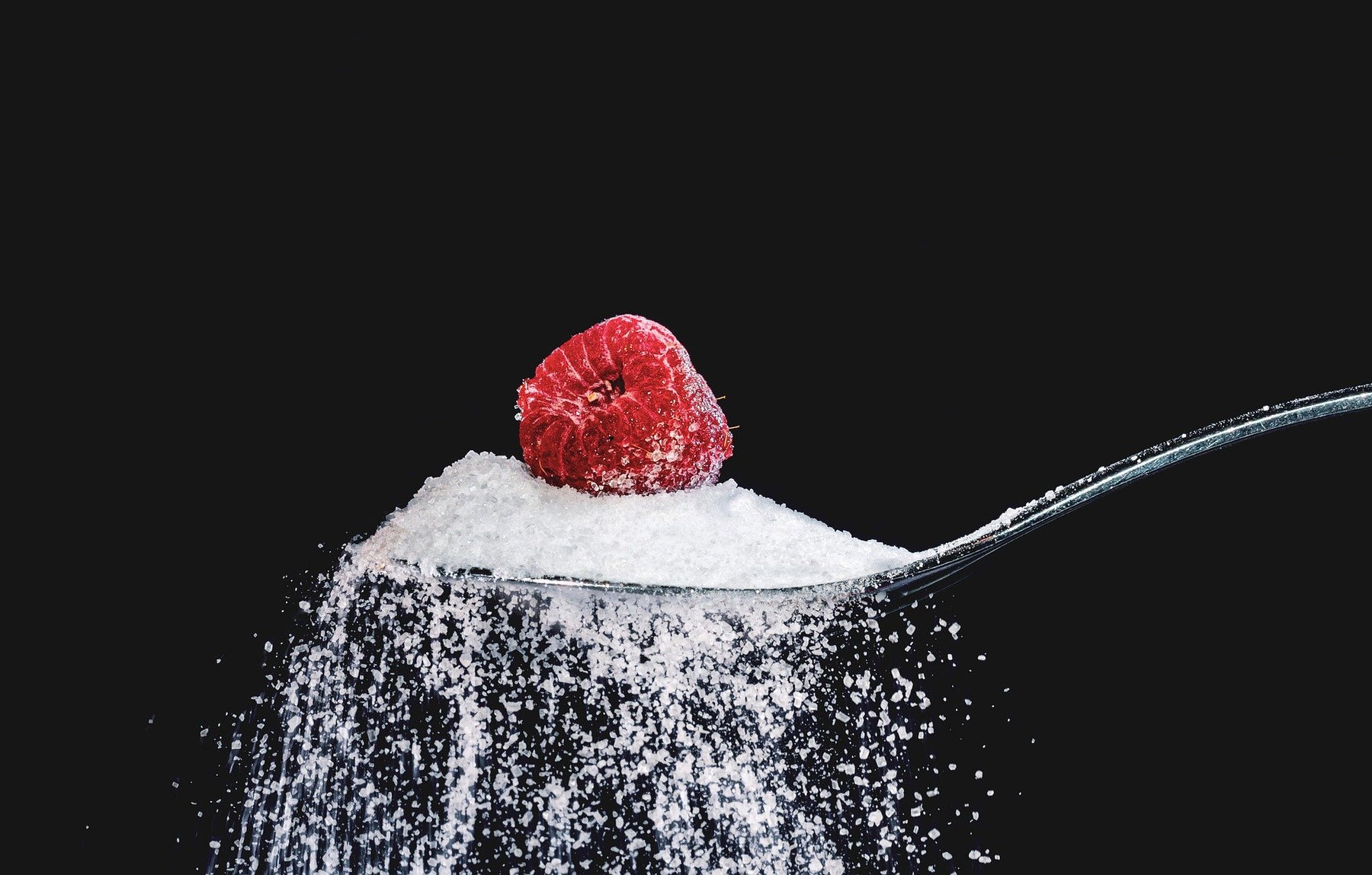 Raspberry above a pile of sugar held by a spoon