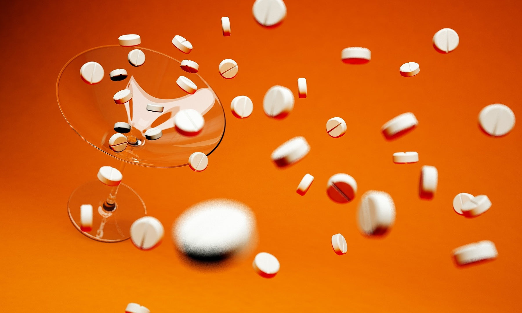Pills falling over an empty glass sitting on an orange floor