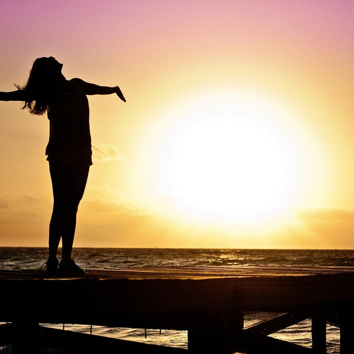 Woman with hands and head up overseeing a sunset over the ocean