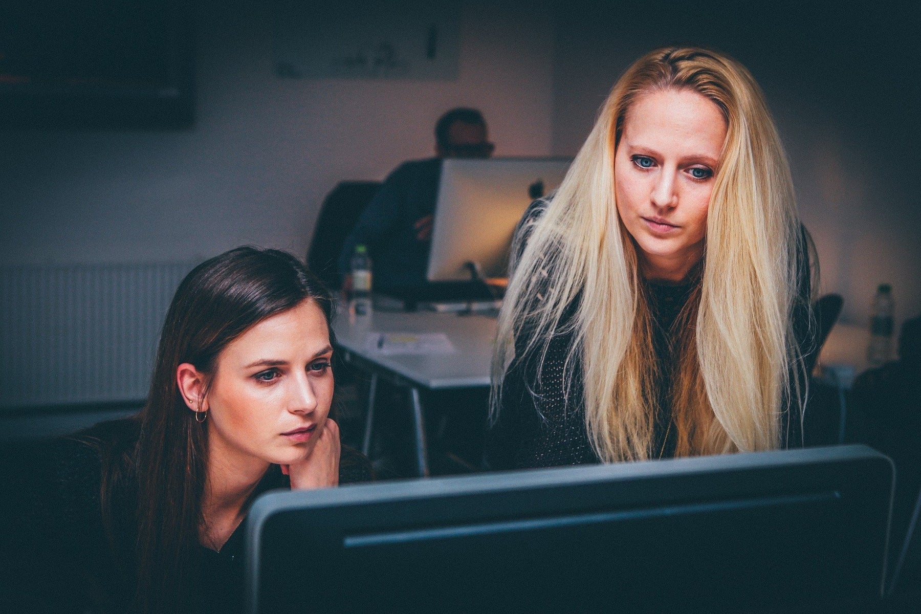 A brunette woman and a blonde woman looking at a screen in an office